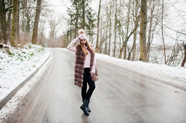 Stylish girl in fur coat and headwear at winter day on road.