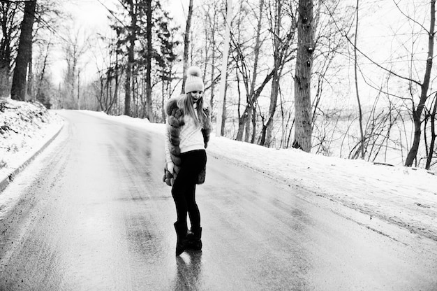 Stylish girl in fur coat and headwear at winter day on road.