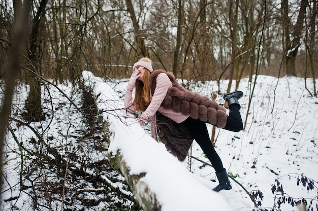 Stylish girl in fur coat and headwear at winter forest.