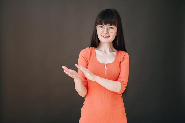 Stylish girl in glasses stands on a black background and claps her hands