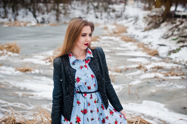 Stylish girl in leather jacket at winter day against frozen lake.