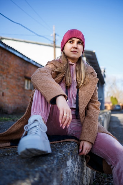 Stylish girl model in a brown coat, pink suit and gray boots on the city ruins. The trends of modern fashion. Fashionable image