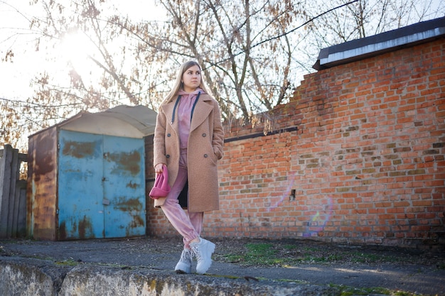 Stylish girl model in a brown coat, pink suit and gray boots on the city ruins. The trends of modern fashion. Fashionable image