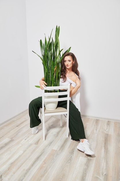 Stylish girl in modern clothes with a green plant on a chair