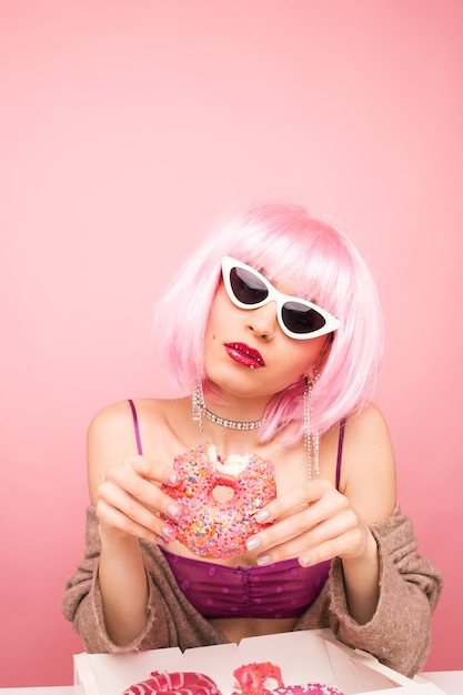 Stylish girl in a pink wig eats delicious donuts on pink