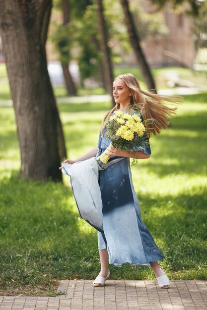 Stylish girl posing in a dress in a sunny spring park. Calm portrait of a beautiful girl standing with a bouquet in spring