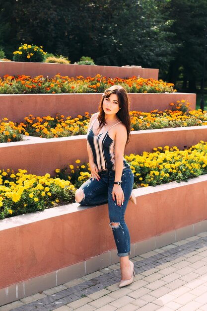 Stylish girl posing near the flowerbeds and looks into the camer