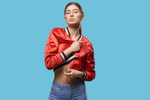 Stylish girl in red bright bomber posing in studio.