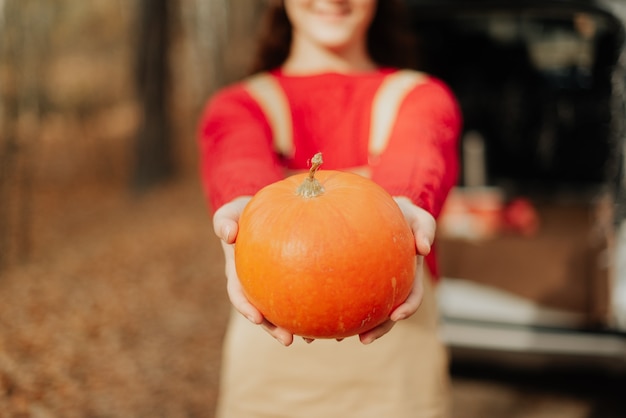 Foto ragazza alla moda in un maglione rosso che tiene un grande primo piano della zucca