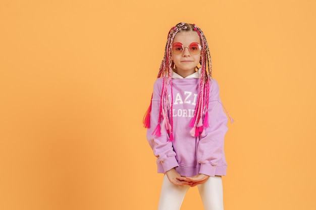 Stylish girl in rounded glasses with pink dreadlocks posing on a yellow background