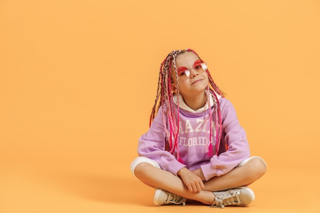 Stylish girl in rounded glasses with pink dreadlocks posing on a yellow background