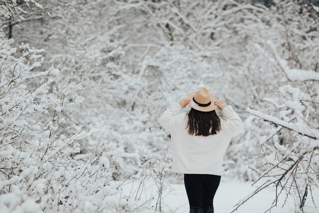 冬の森の雪に覆われた木々の間に立って、雪の時間を楽しんでいるスタイリッシュな女の子。