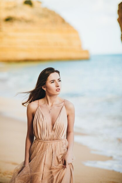 stylish girl standing with flying hair from the wind at sunset on the beach and the ocean