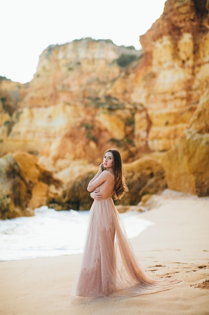 stylish girl standing with flying hair from the wind at sunset on the beach and the ocean