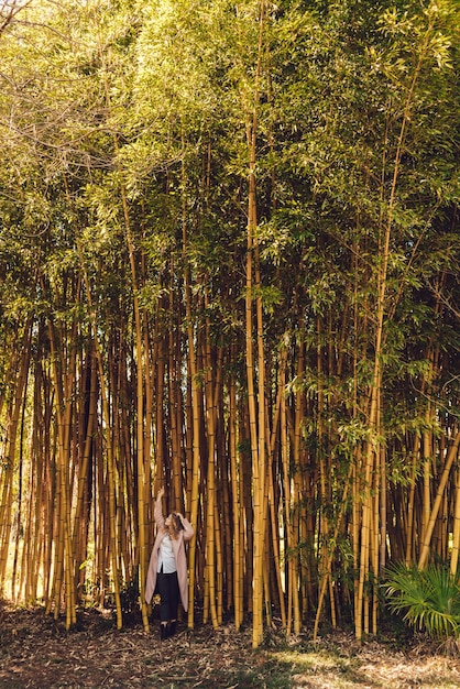 背の高い竹の木を背景にポーズをとってトレンディなコートを着たスタイリッシュな女の子