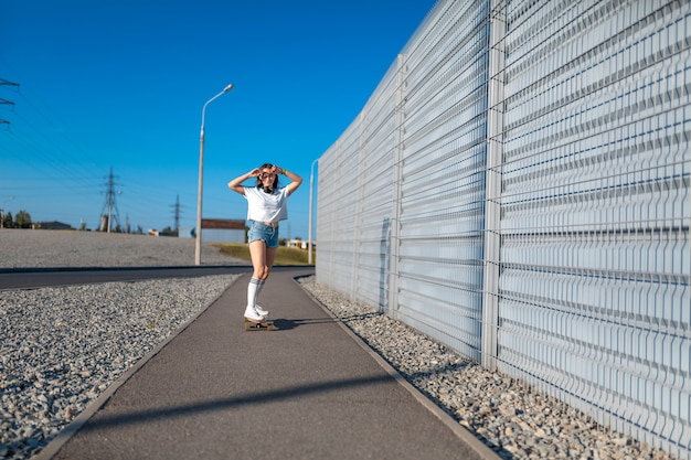 Stylish girl in white stockings ride on longboard down the street and listening music