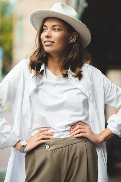 Stylish girl in white trousers and white cotton blouse posing against the wall