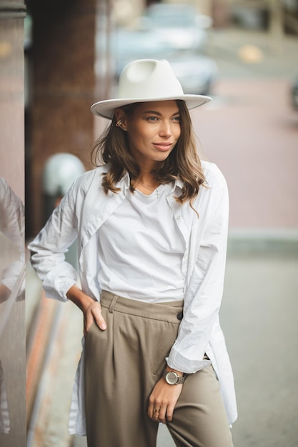 Stylish girl in white trousers and white cotton blouse posing against the wall