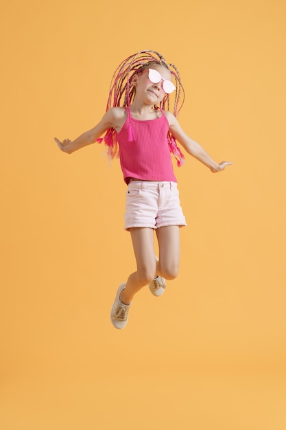 Stylish girl with pink dreadlocks jumping on a yellow background