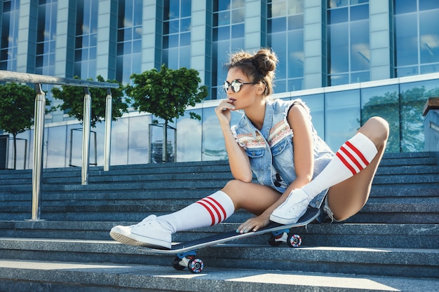 Foto ragazza alla moda con uno skateboard sulla strada