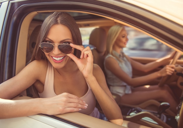 Стильные девушки улыбаются и веселятся за рулем автомобиля.