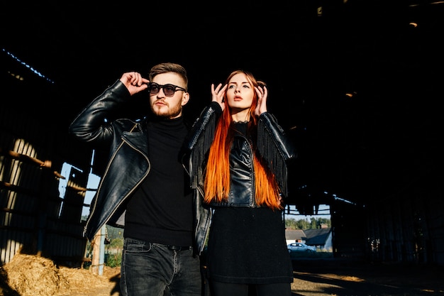 Stylish glamorous couple in black leather jackets posing in a hangar