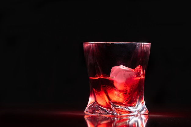 Stylish glass of red rum on ice illuminated