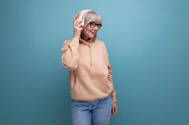 Stylish grandmother with gray hair masters technique and listens to music in headphones on a studio