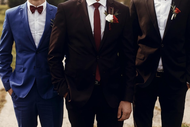 Stylish groom with groomsmen in suits with boutonniere posing getting ready in morning for wedding ceremonyxa