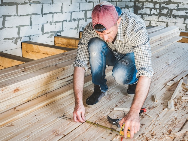 Ragazzo alla moda in un berretto da baseball, jeans e una maglietta, lavorando con strumenti su legno all'interno della casa in costruzione. concetto di costruzione e riparazione