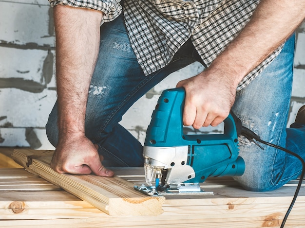 Stylish guy in a baseball cap, jeans and a shirt, working with tools on wood inside the house under construction. Concept of construction and repair