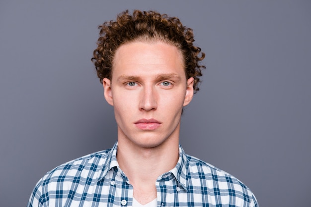 Stylish guy in a blue checkered shirt posing against the grey wall