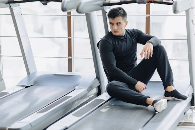 Stylish guy in the gym sits resting on the treadmill