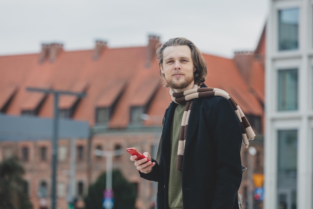 Photo stylish guy in scarf and coat hold mobile phone in a hand at street of wroclaw poland