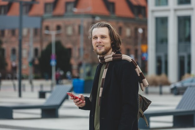 Ragazzo alla moda in sciarpa e cappotto tiene il telefono cellulare in mano in una strada di wroclaw in polonia