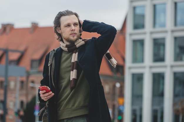 Photo stylish guy in scarf and coat hold mobile phone in a hand at street of wroclaw poland