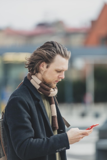 Photo stylish guy in scarf and coat hold mobile phone in a hand at street of wroclaw poland