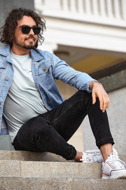 A stylish guy with glasses stone wall on the background and looks away strong and strict male in casual clothes