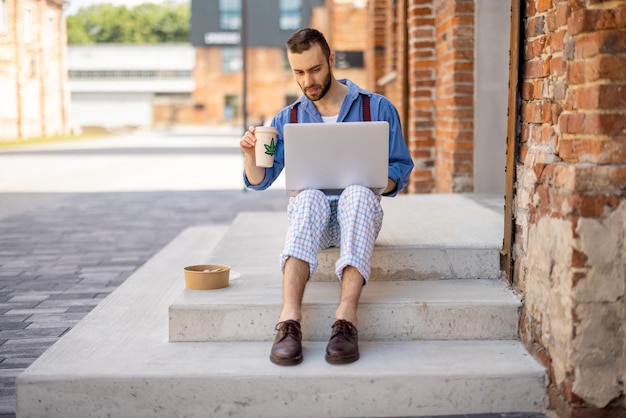 Stylish guy works on laptop computer on a street