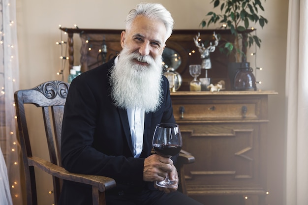 Uomo anziano barbuto elegante e bello che beve vino rosso