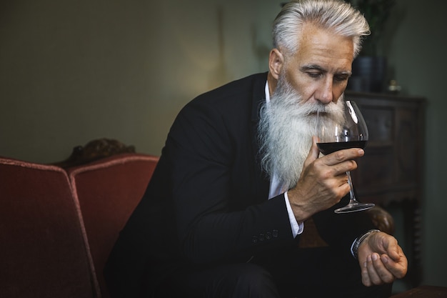 Stylish and handsome bearded senior man drinking red wine