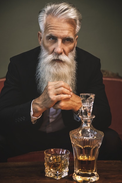 Foto uomo anziano barbuto elegante e bello che beve whisky