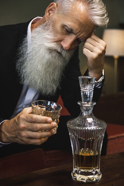 Стильный и красивый бородатый старший мужчина пьет виски