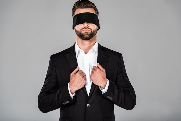 Stylish handsome blindfolded businessman in black suit isolated on grey