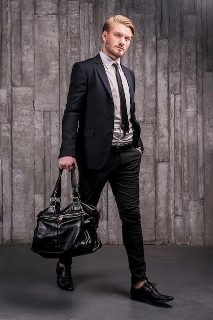 Stylish handsome. Full length of handsome young man in formalwear carrying a black bag