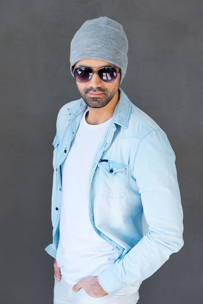 Stylish handsome. Handsome young man in eyewear and headwear posing against grey background