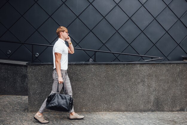 Uomo bello alla moda che cammina sulla strada vicino alla moderna costruzione nera.