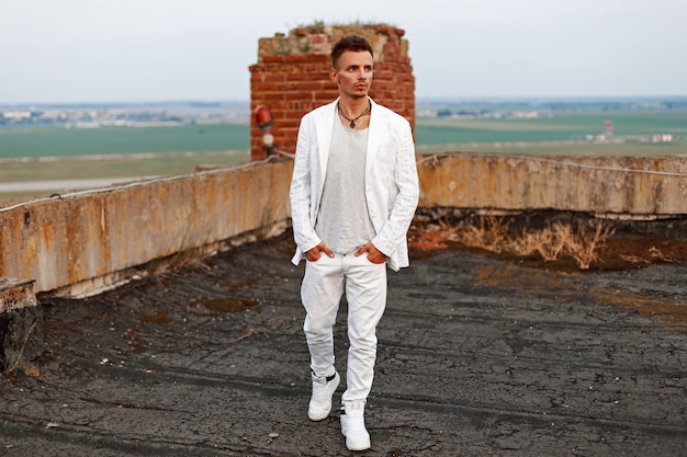 Uomo bello alla moda in una maglietta bianca, jeans e scarpe che camminano sul tetto.