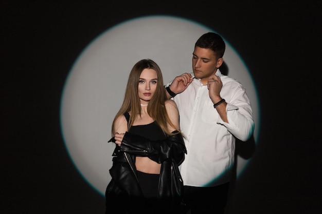 Stylish handsome young couple beautiful girl and handsome man in fashion clothes on a dark background in a light circle