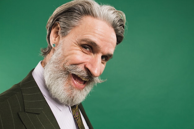 Stylish and happy bearded middle-aged man in suit closeup on green wall